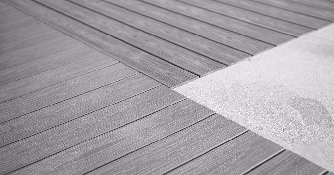 Nahaufnahme einer Holzterrasse mit parallelen Dielen, die an eine glatte, helle Fläche angrenzen.