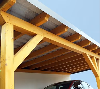 Holzcarport mit rotem Auto unter blauem Himmel.