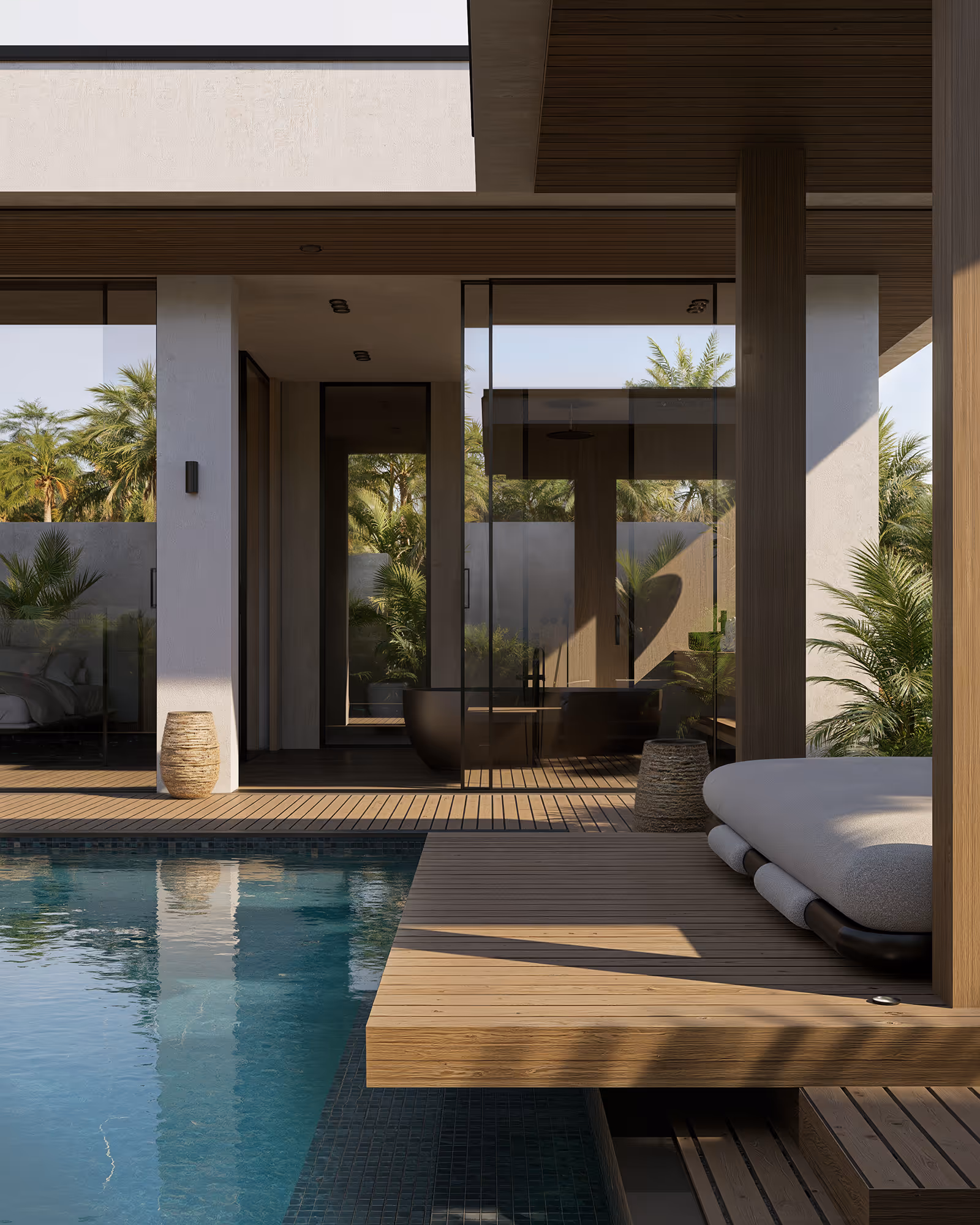 Modern outdoor pool area with wooden deck, cushioned lounge bed, and glass-walled interior featuring plants and a black bathtub.