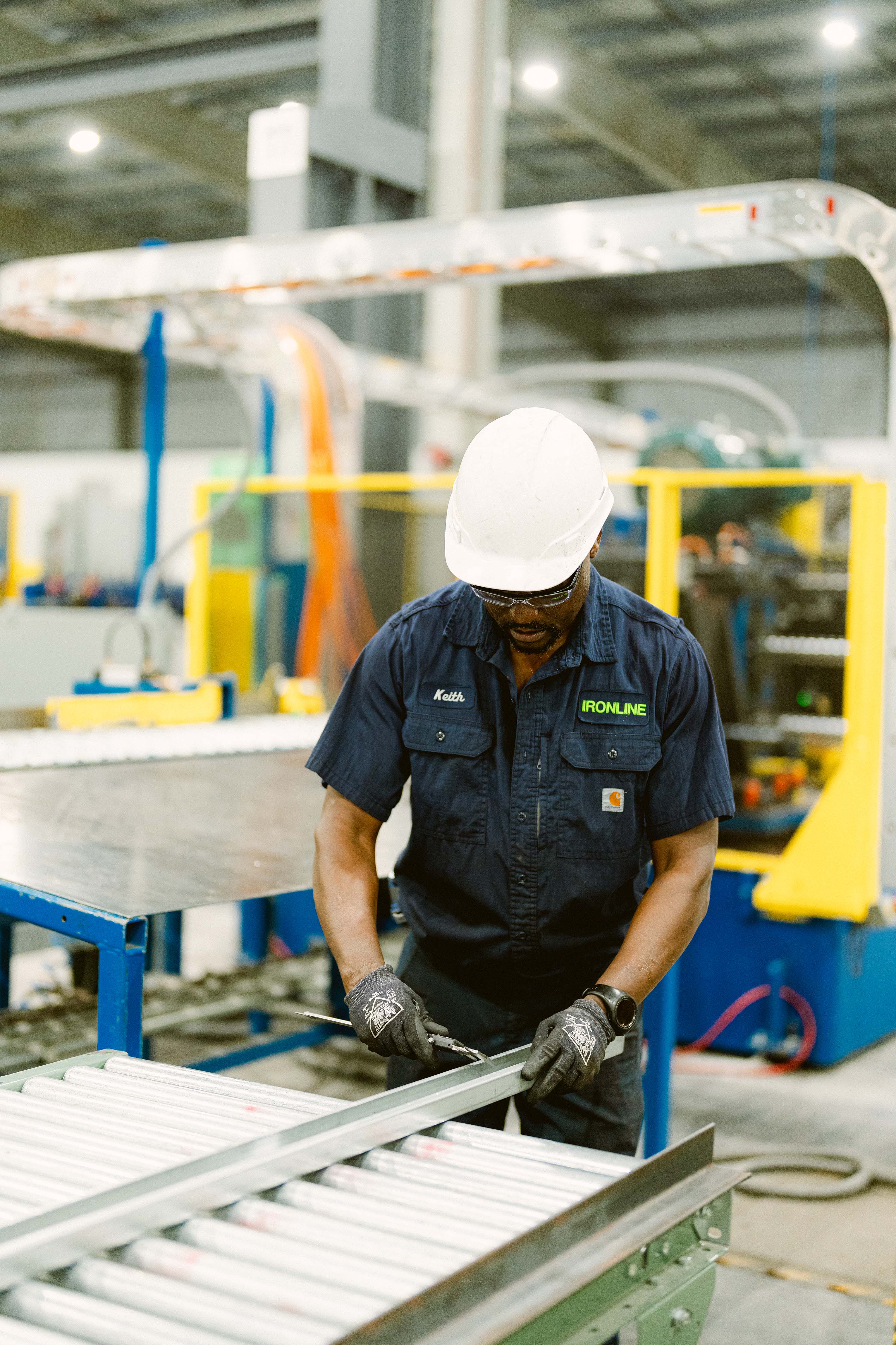 Industrial worker wearing a hard hat and gloves measuring a metal sheet at a factory.