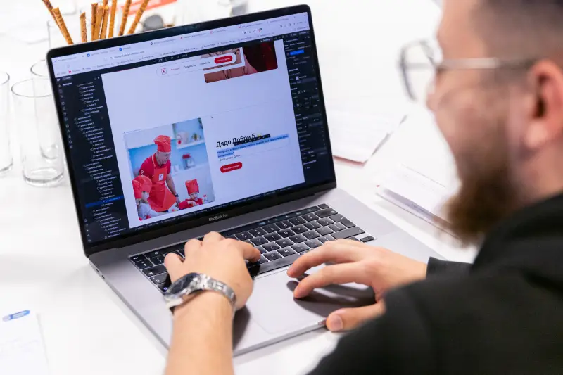 Person with beard and glasses working on a laptop web design showing chefs in red uniforms.