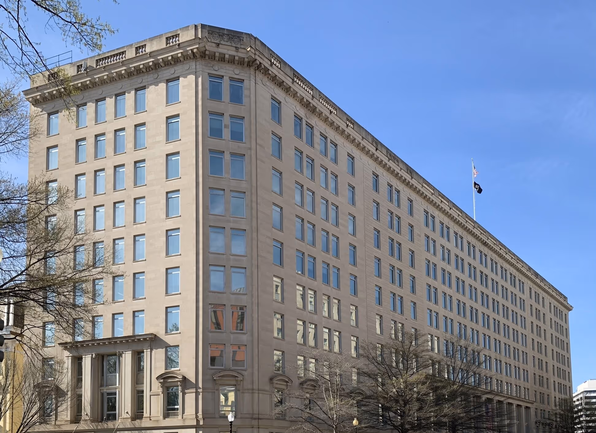 Large multi-story government building with many windows and American flags on the roof against a clear blue sky.