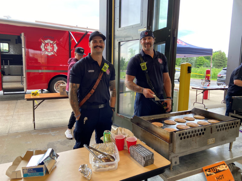 Firefighter wearing full gear and helmet cutting a wooden beam with a power saw, sending sparks flying.