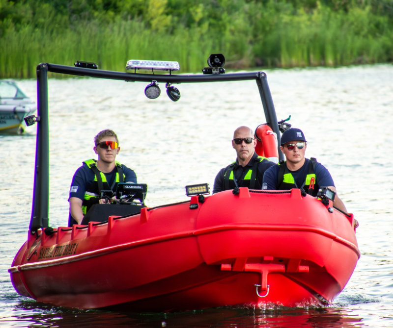 Firefighter wearing full gear and helmet cutting a wooden beam with a power saw, sending sparks flying.
