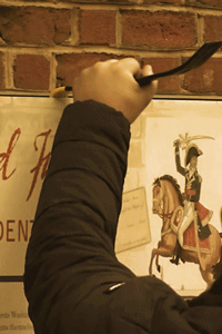 Person using a crowbar to remove or pry a historic sign mounted on a brick wall at a National Park.