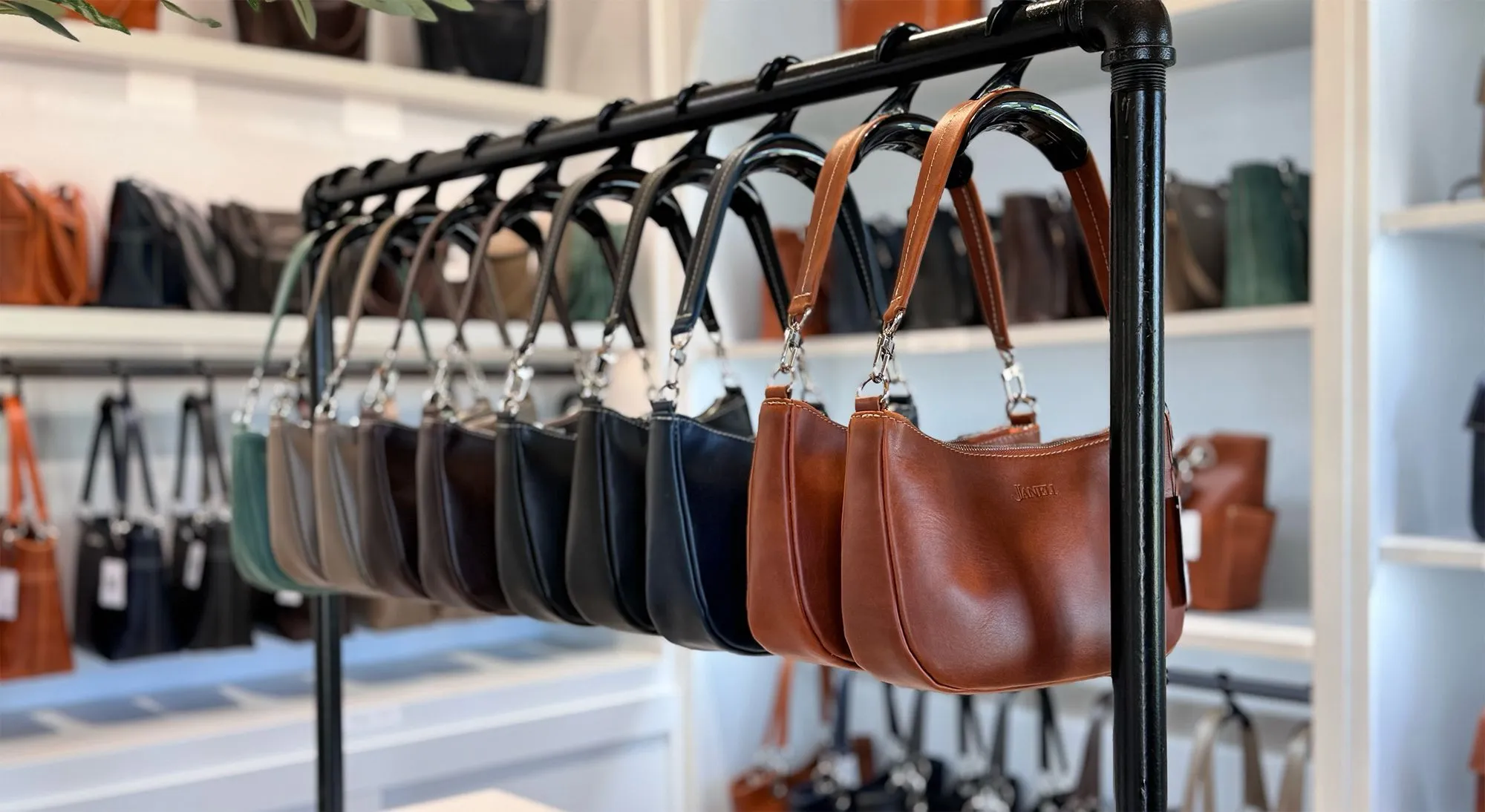 Leather handbags in various colors displayed hanging on a metal rack in a store.