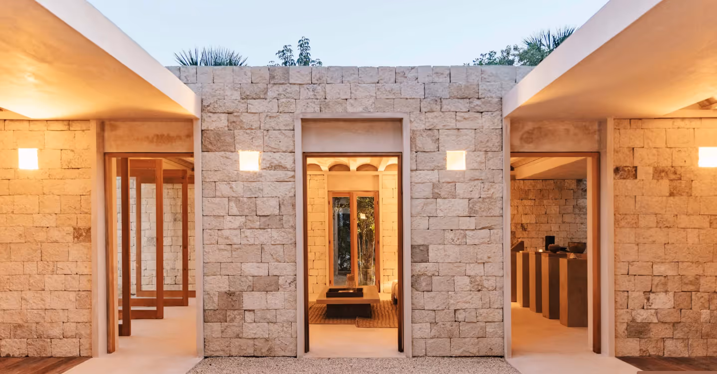 Modern stone house exterior with three doorways and warm interior lighting at dusk.