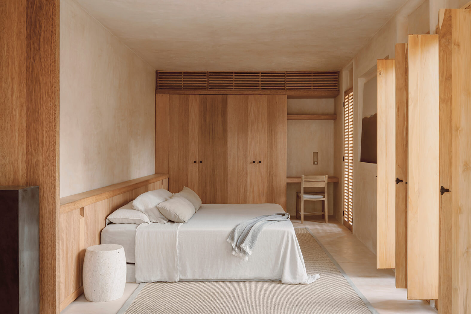 Minimalist bedroom with light wood furniture, beige bed linens, and a neutral rug.
