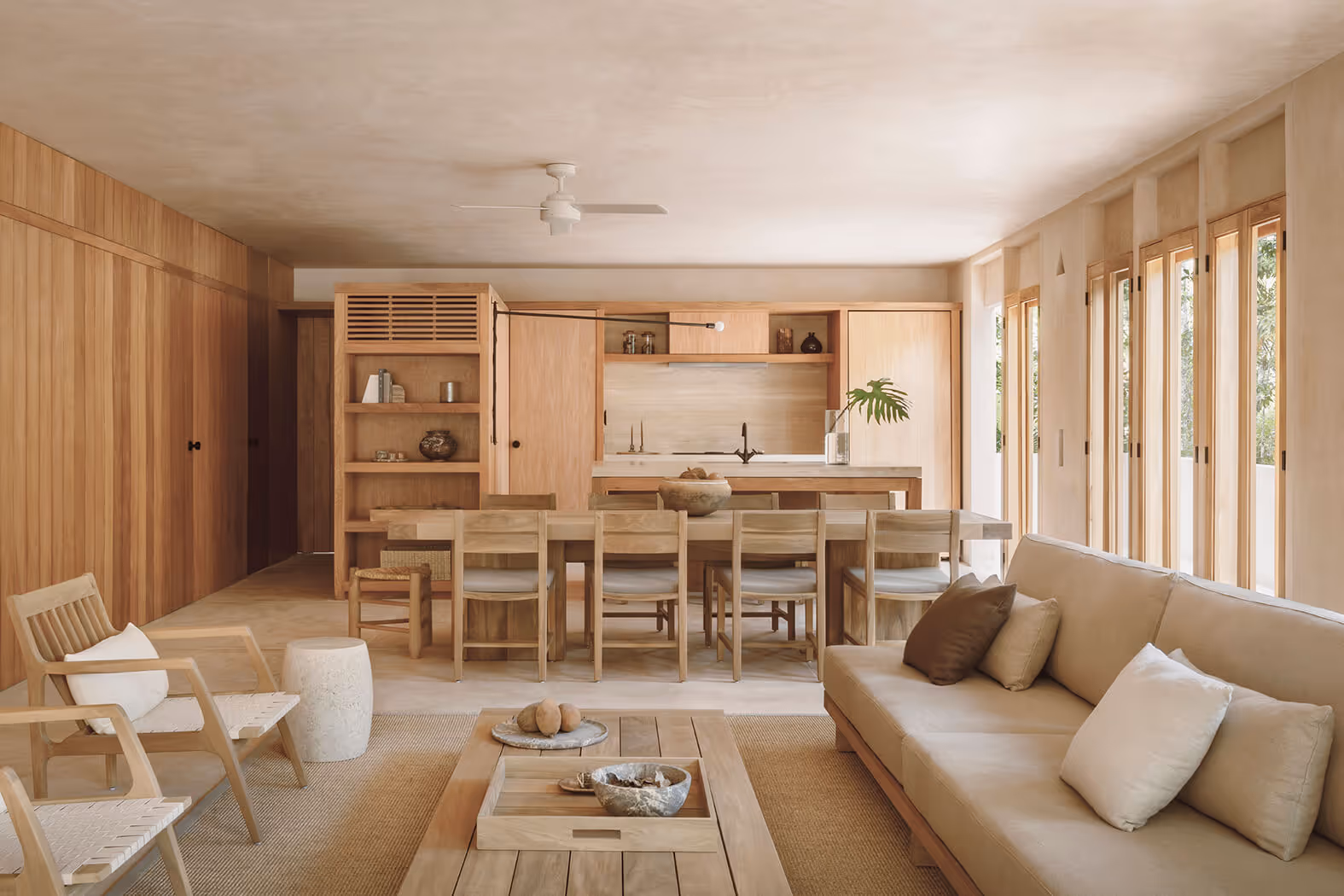 Minimalist open-plan living and dining area with light wood furniture, beige sofa, and large windows letting in natural light.