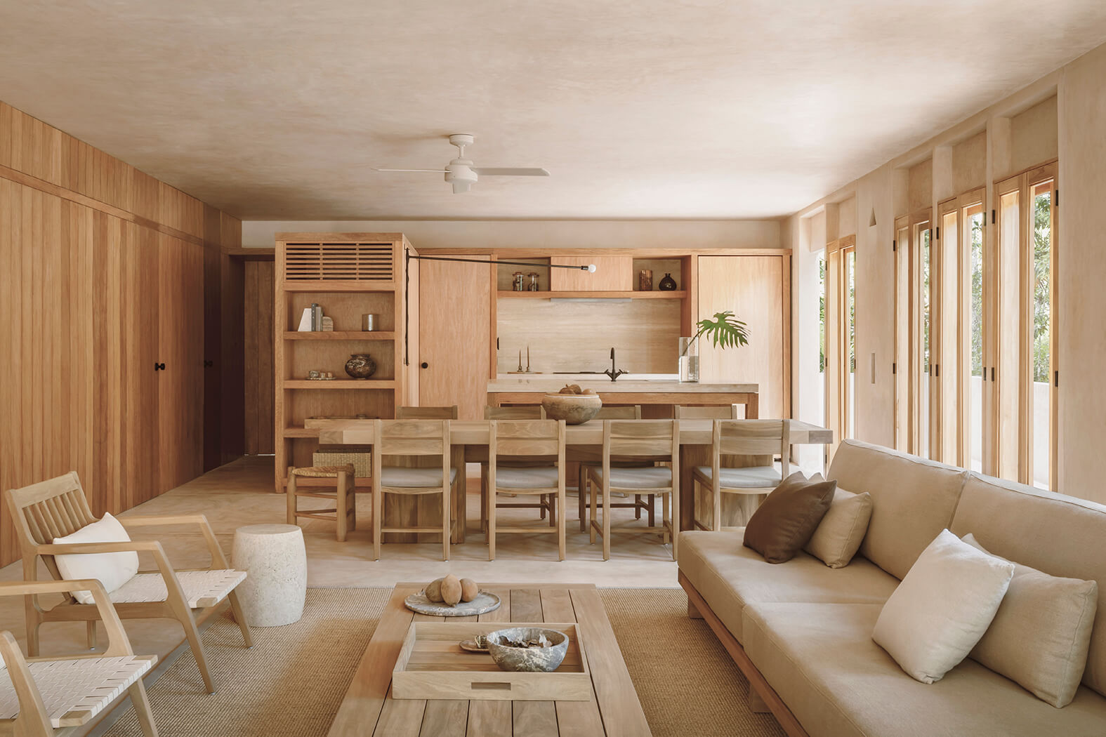 Minimalist open-plan living and dining area with light wood furniture, beige sofa, and large windows letting in natural light.
