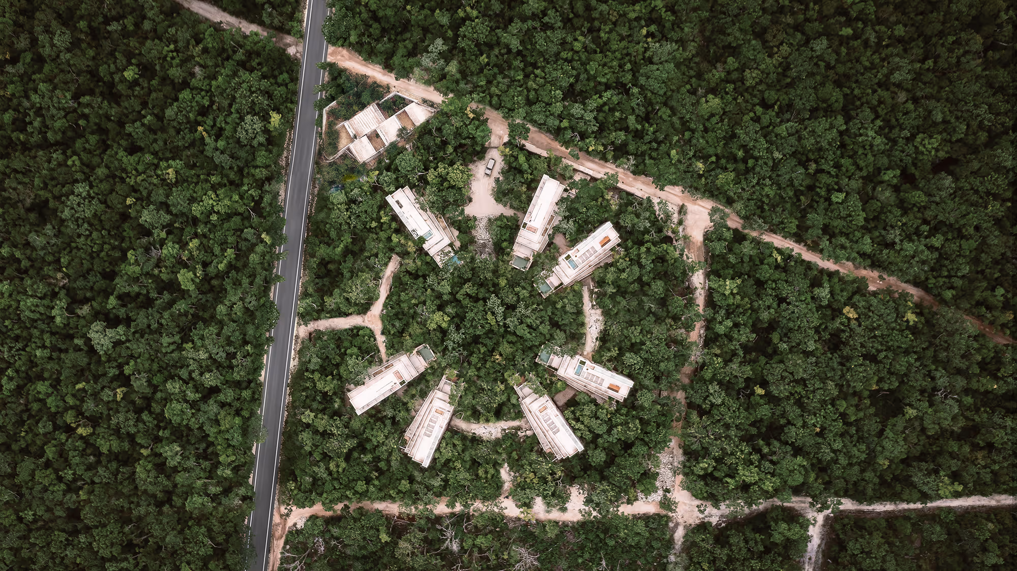 Aerial view of eight modern rectangular buildings arranged in a circle surrounded by dense forest.
