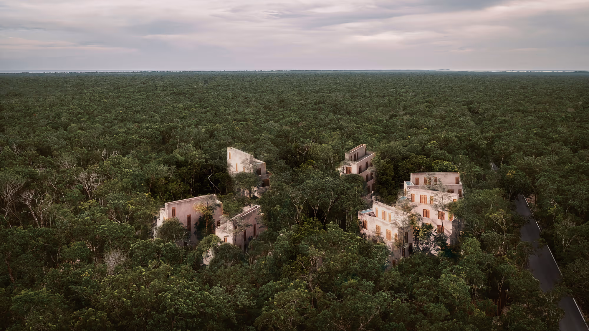 Several modern buildings partially hidden by dense forest under a cloudy sky.