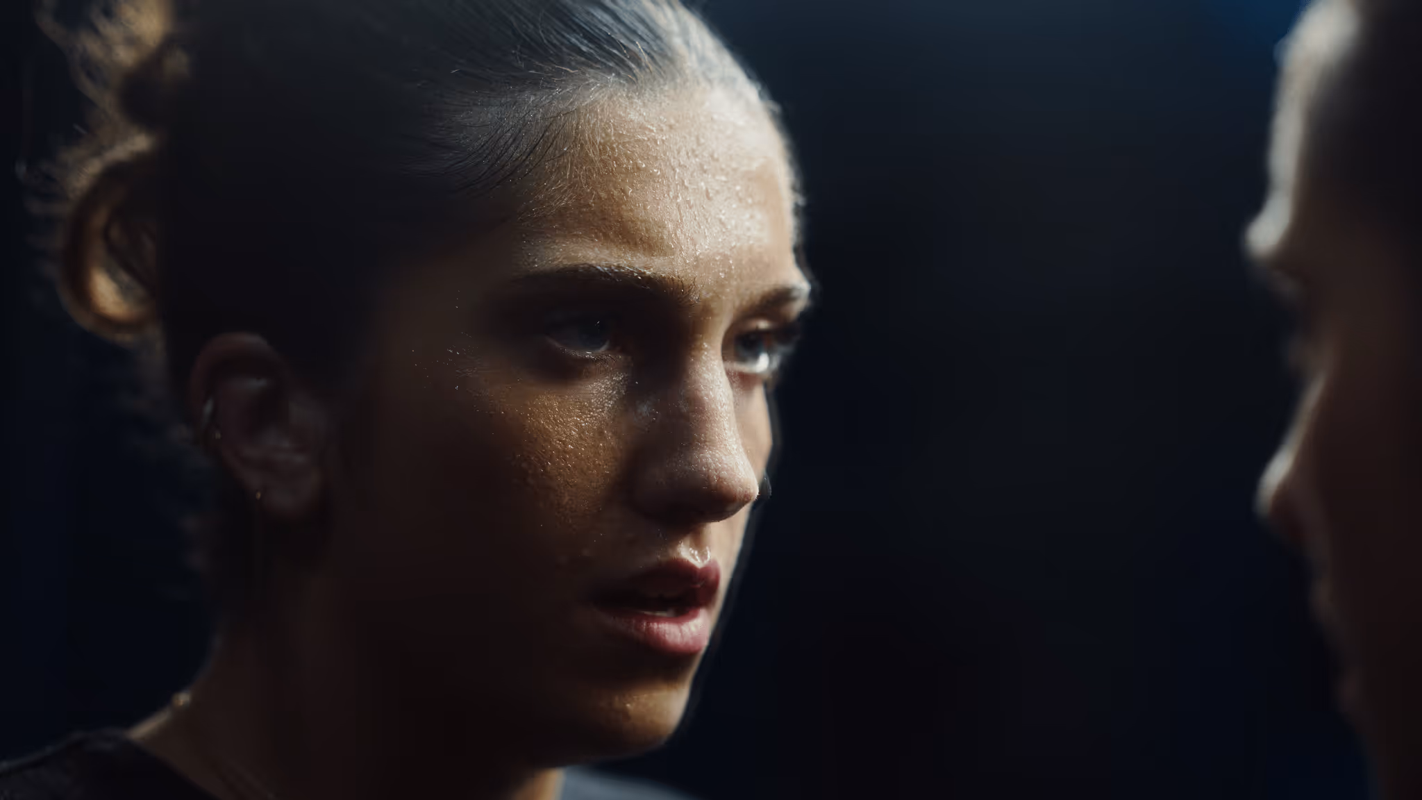 Close-up of a woman with sweat on her face, looking intently at herself in the mirror.