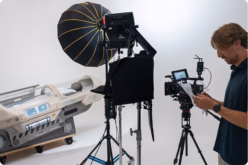 Man reviewing notes next to professional camera and lighting equipment in a white studio with a futuristic pod containing a person inside.