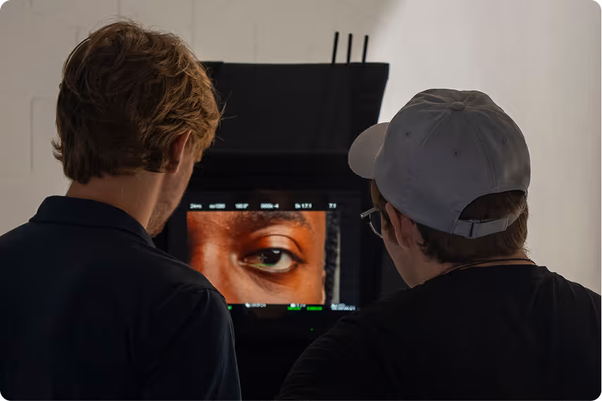Two men viewed from behind looking at a monitor displaying a close-up of a person's eye in a studio setting.
