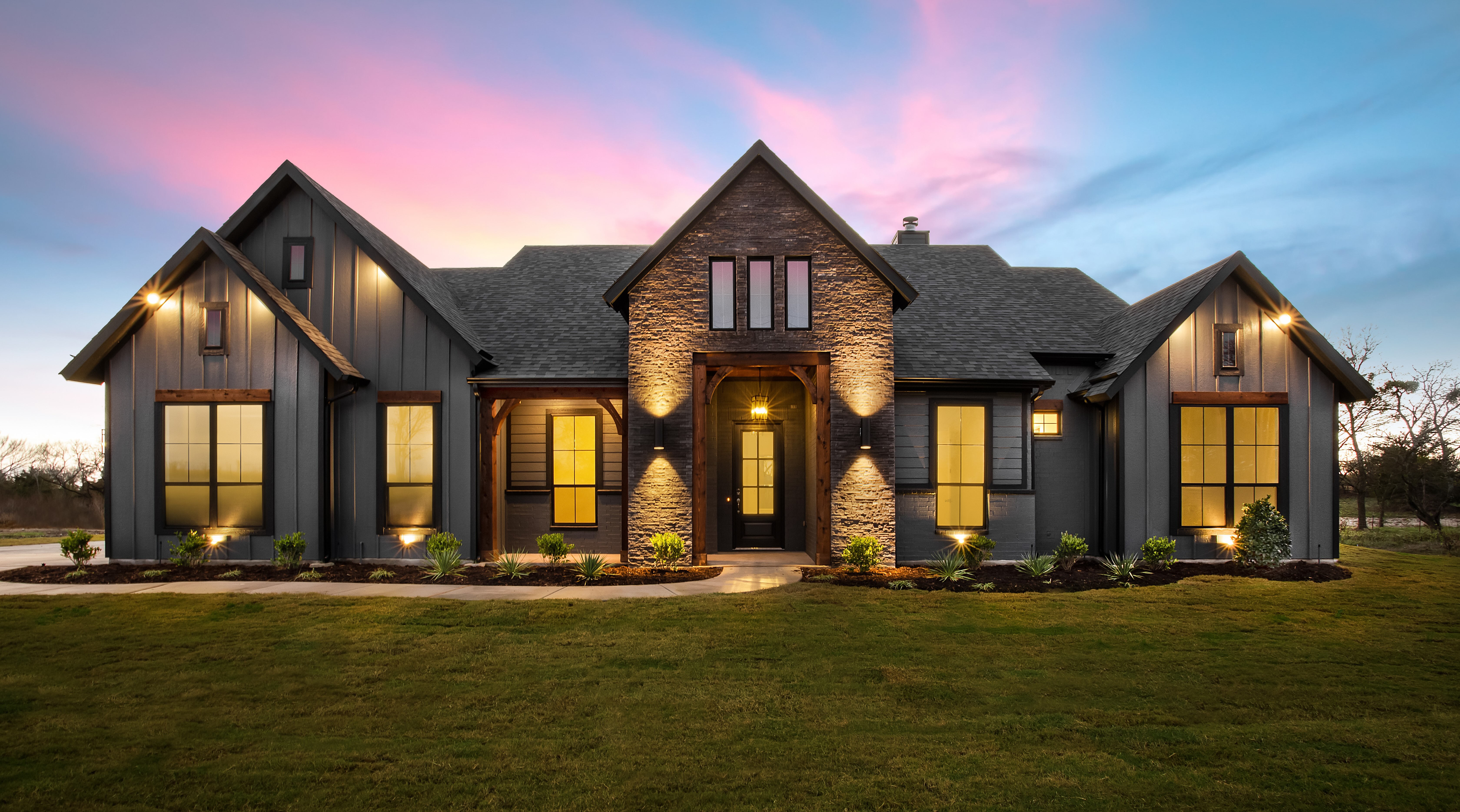 Custom home exterior at sunset dramatic dusk sky stone and timber facade