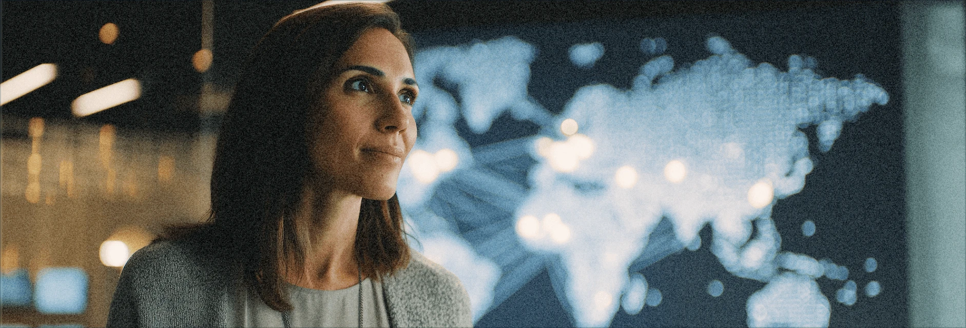 Thoughtful woman looking at a digital world map with illuminated connection points in a dimly lit office.
