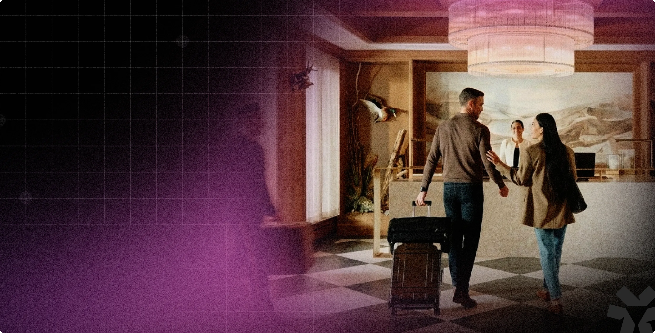 Couple entering hotel lobby with luggage, greeted by a receptionist behind the front desk.