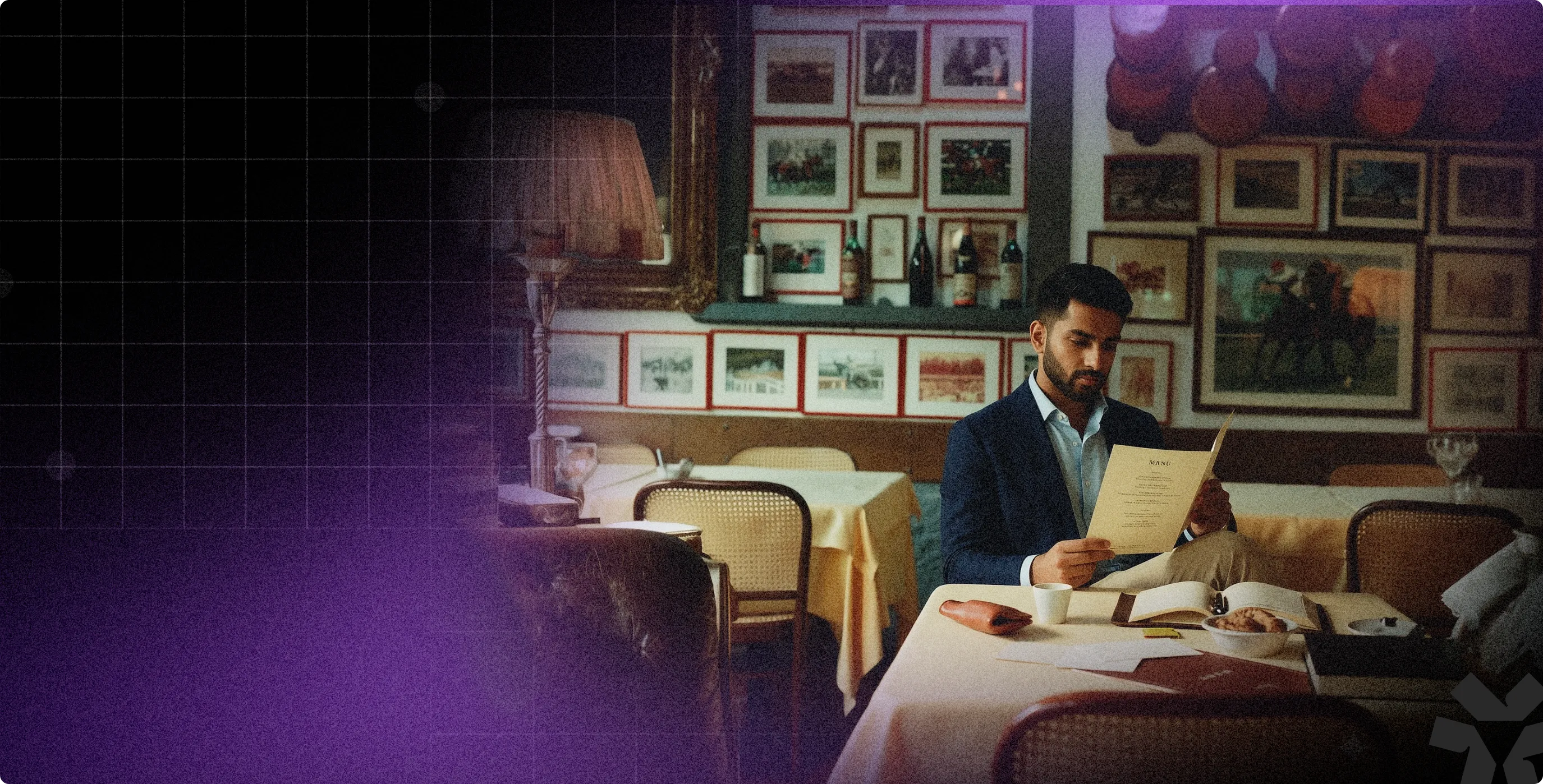 Man in a dark blue blazer sitting at a restaurant table reading a menu surrounded by framed pictures on the wall.
