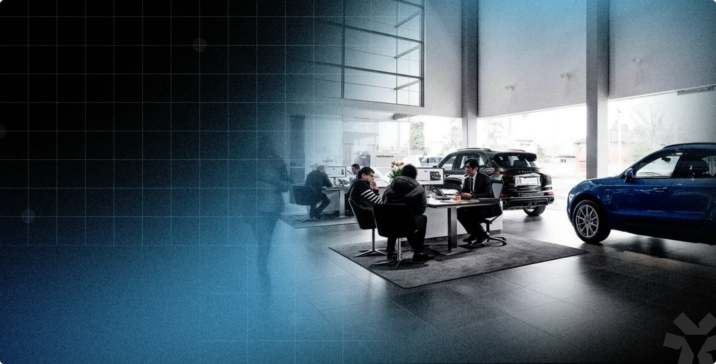 Car dealership showroom with customers seated at desks discussing with sales representatives near displayed vehicles.