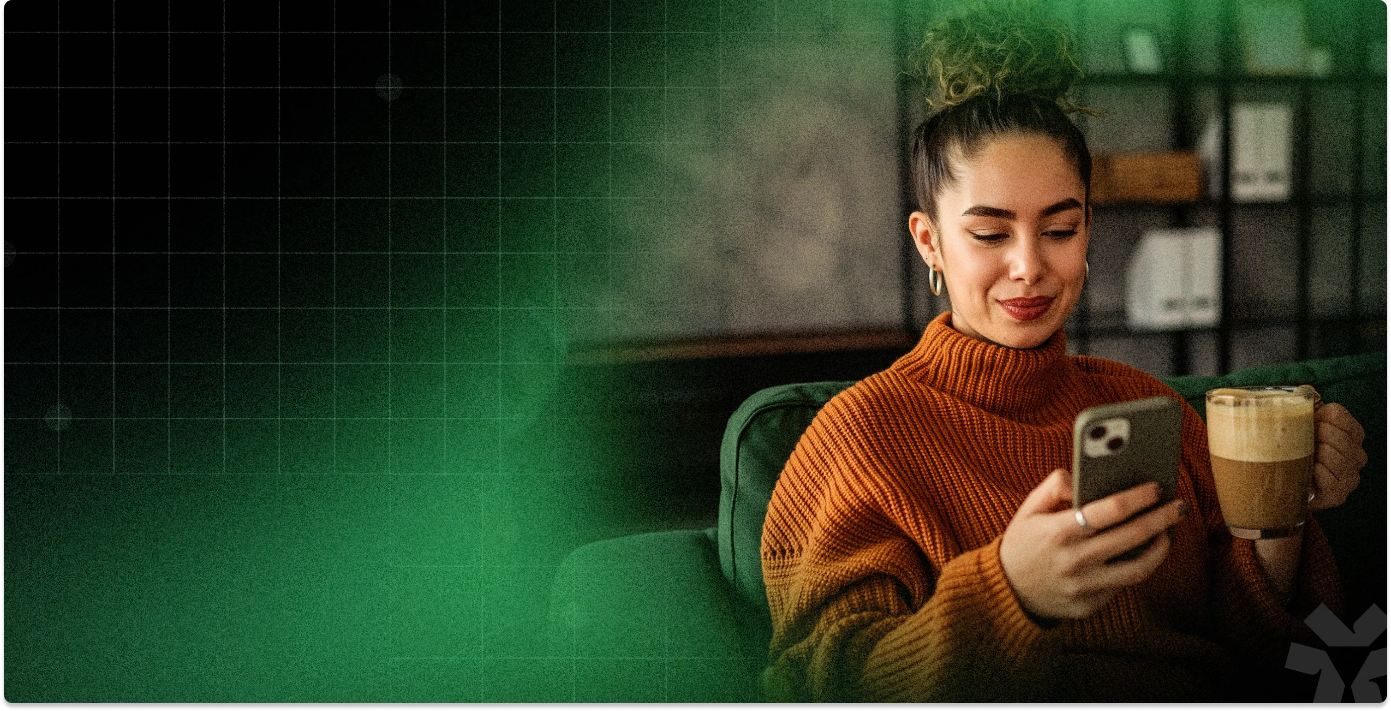 Woman in orange sweater sitting on a green couch, holding a coffee and looking at her smartphone.