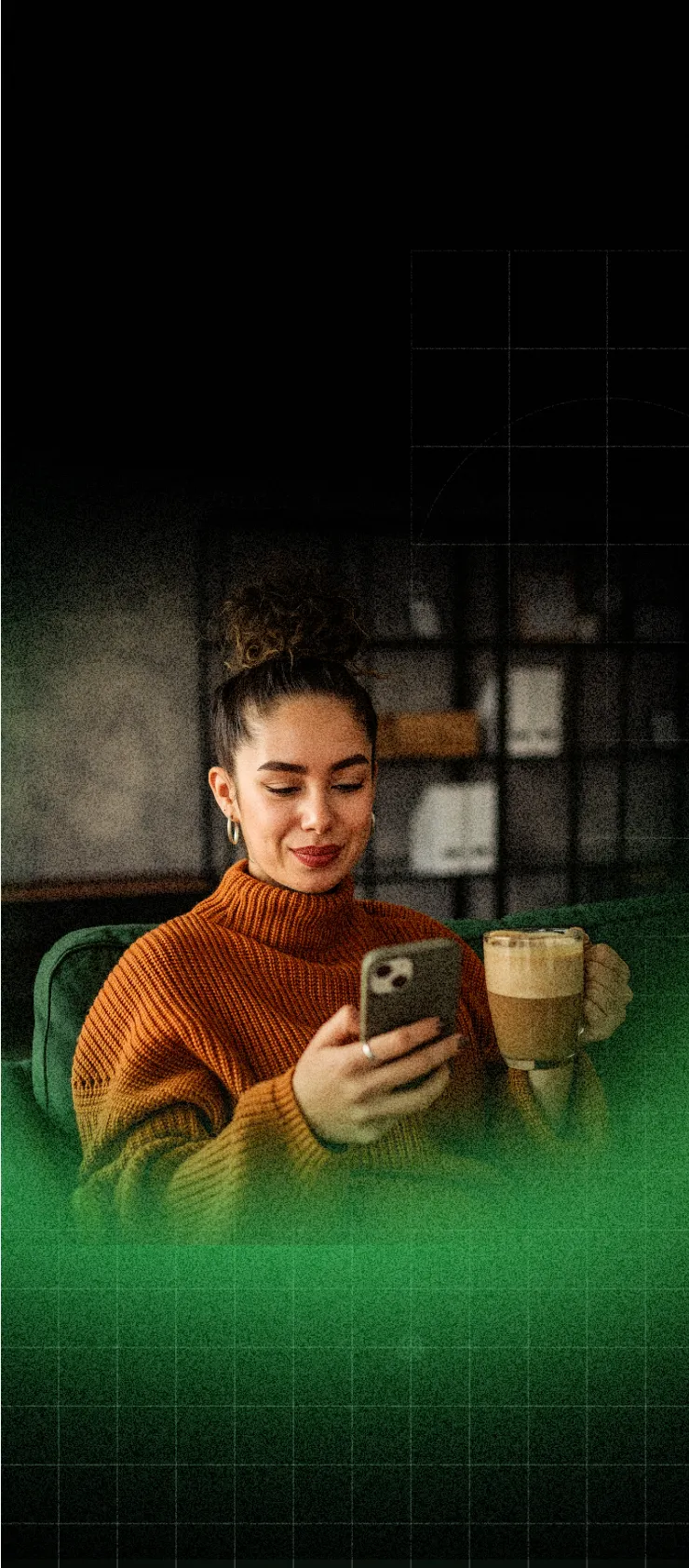 Young woman in an orange sweater sitting on a green couch, holding a coffee cup and looking at her smartphone with a slight smile.
