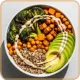 Bowl with grilled chicken, chickpeas, avocado slices, broccoli, and quinoa on a light surface.