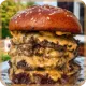 Stacked cheeseburger with multiple beef patties, melted cheese, and a sesame seed bun.
