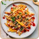 Plate of loaded fries topped with melted cheese, diced tomatoes, green herbs, and ketchup drizzle.