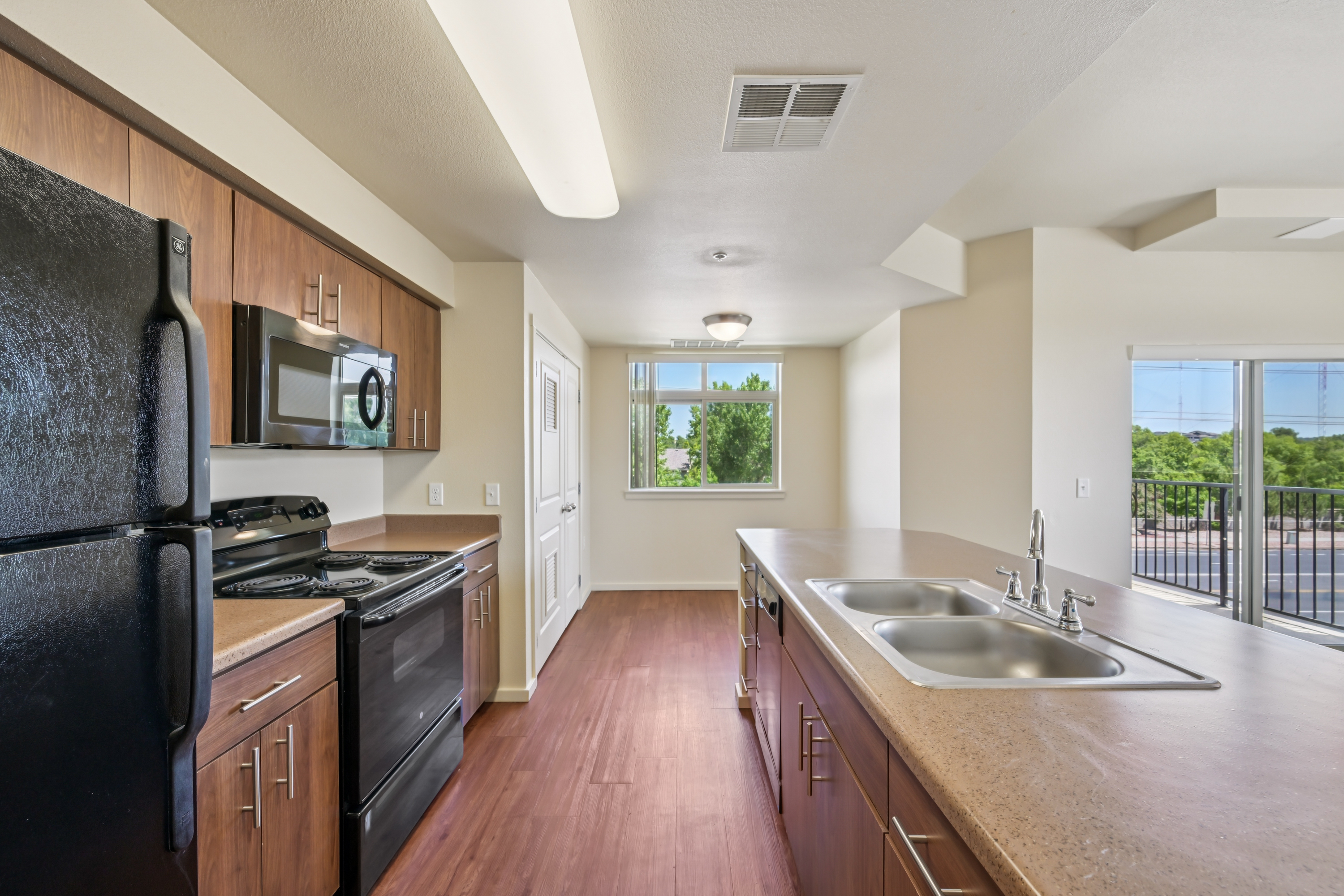 Modern kitchen with breakfast bar, black appliances, and wood-style cabinetry at Copper Creek Apartments