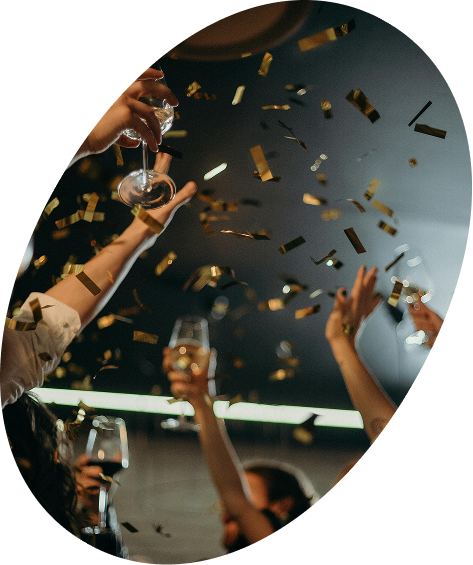 Group of people raising wine glasses in celebration with gold confetti falling.