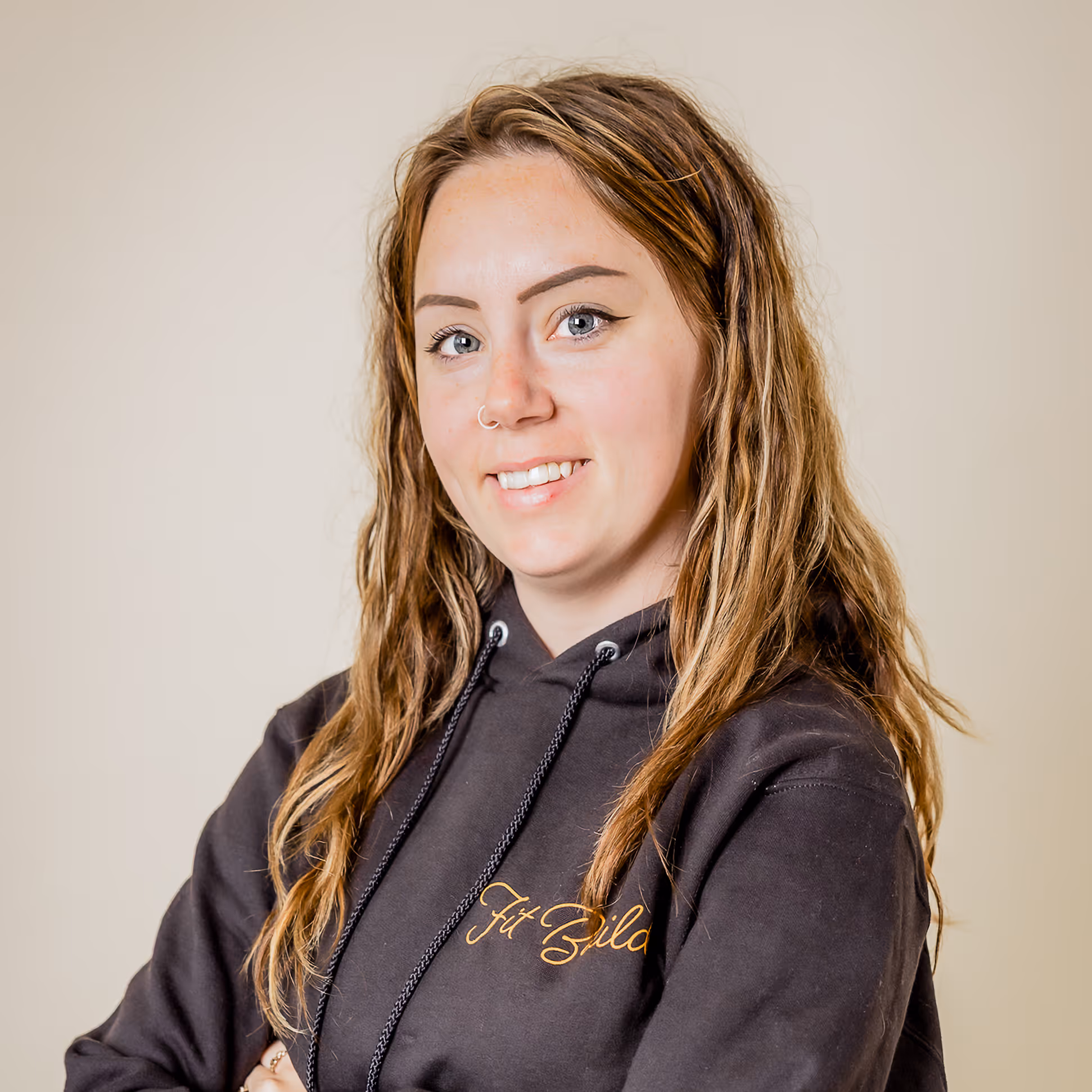 Smiling young woman with wavy light brown hair wearing a dark hoodie with yellow cursive text.