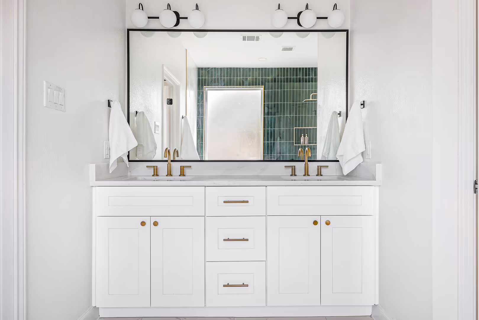 Austin modern white bathroom vanity with dual gold faucets, a large rectangular mirror, and two white towels hanging on each side.