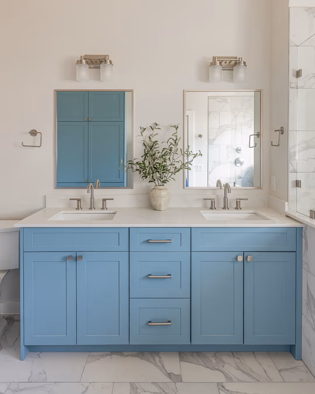 Modern bathroom with double blue vanity, white countertop, two mirrors, and a vase with green branches in the center, in Austin.