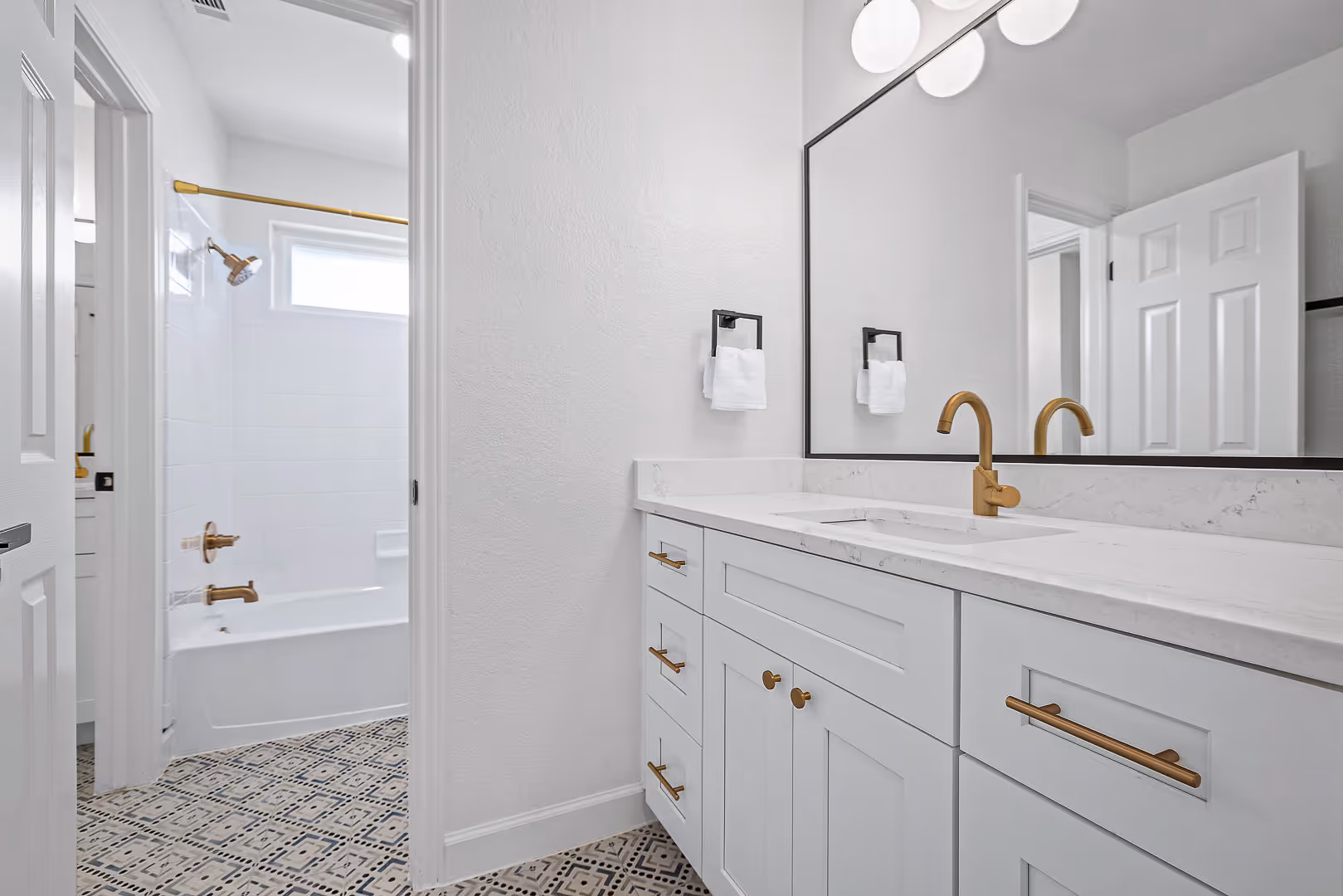 Modern bathroom design with white cabinetry, brass fixtures, large mirror, and patterned tile floor, Austin.