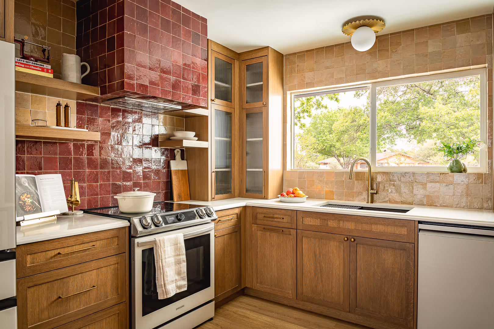 Modern remodeled kitchen with wooden cabinets, white countertops, a stainless-steel stove, and a large window overlooking green trees.