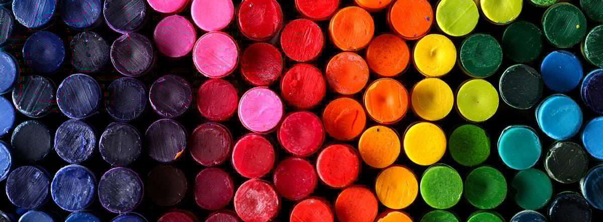 Close-up of circular paint sticks arranged in a gradient of colors from dark purple and blue to pink, red, orange, yellow, green, and blue.