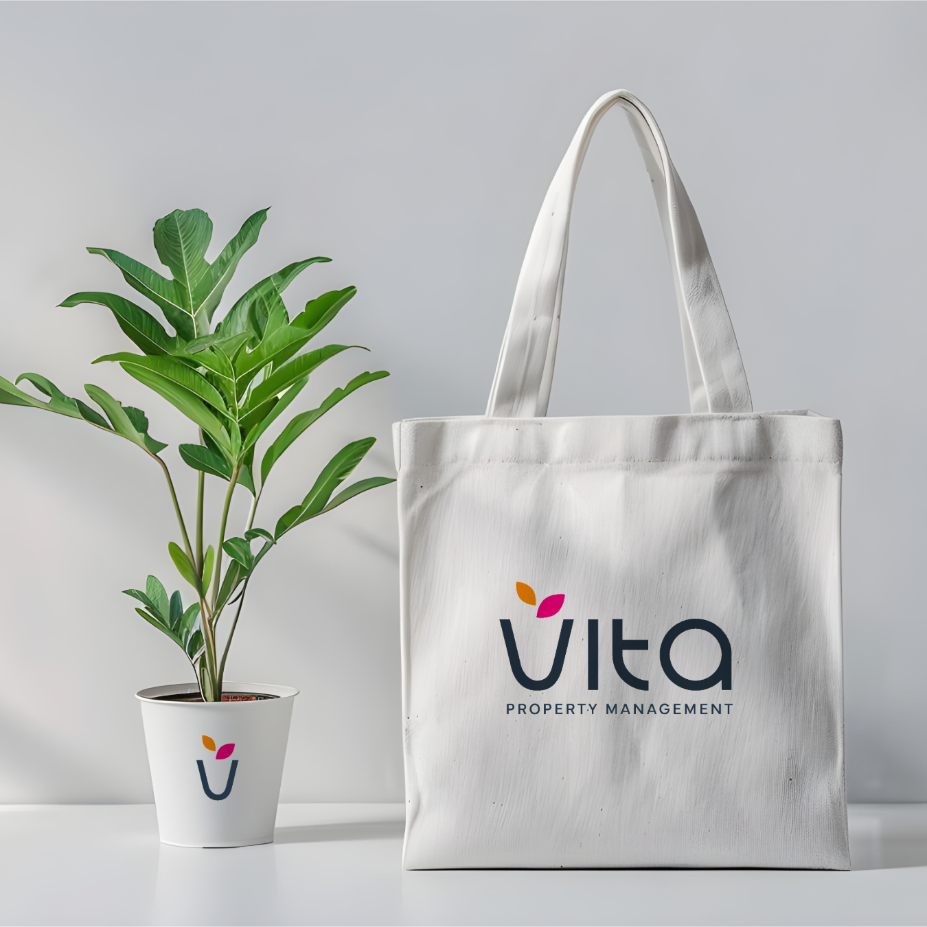 White tote bag and white plant pot with green leafy plant, both featuring the Vita Property Management logo.