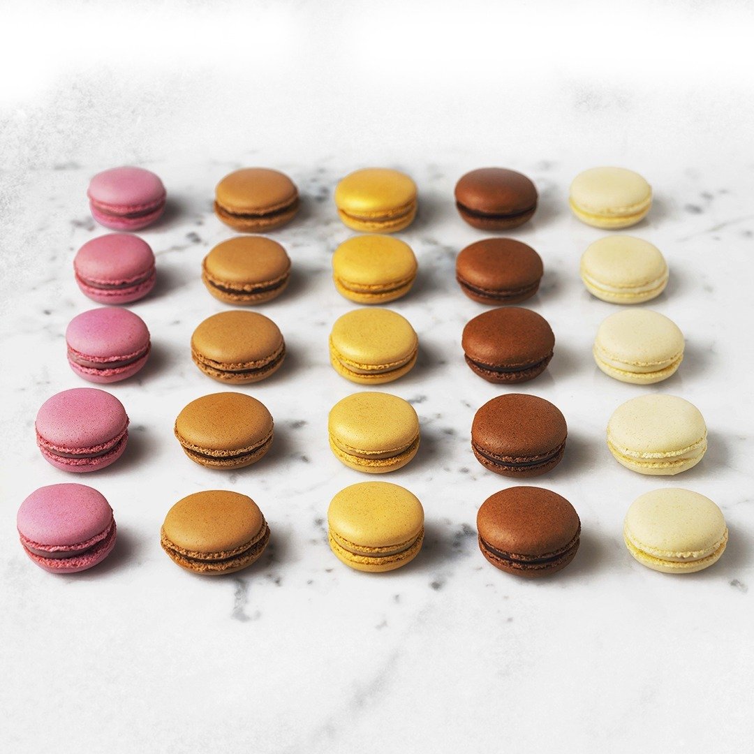Five rows of colorful macarons in pink, brown, yellow, chocolate, and cream arranged neatly on a white marble surface.