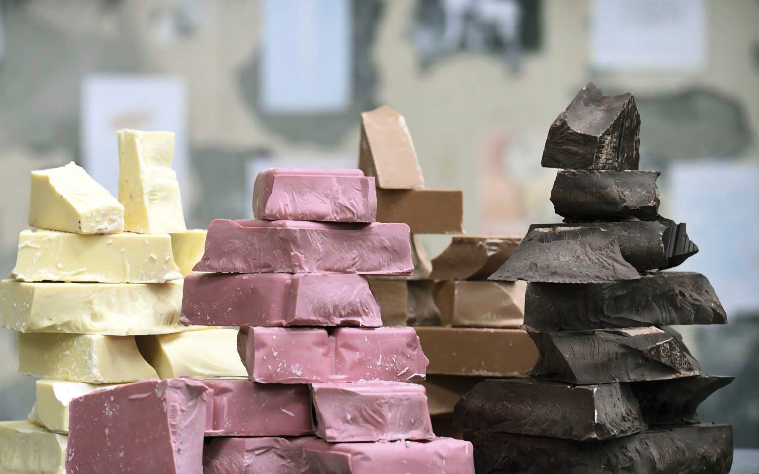 Stacks of chunks of white, pink, milk, and dark chocolate against a blurred background.