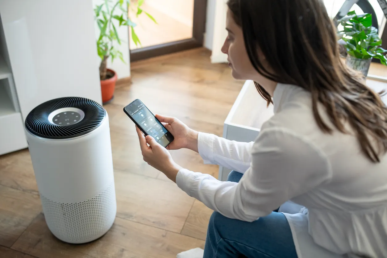 A person sits on a sofa looking at their phone next to an air purifier