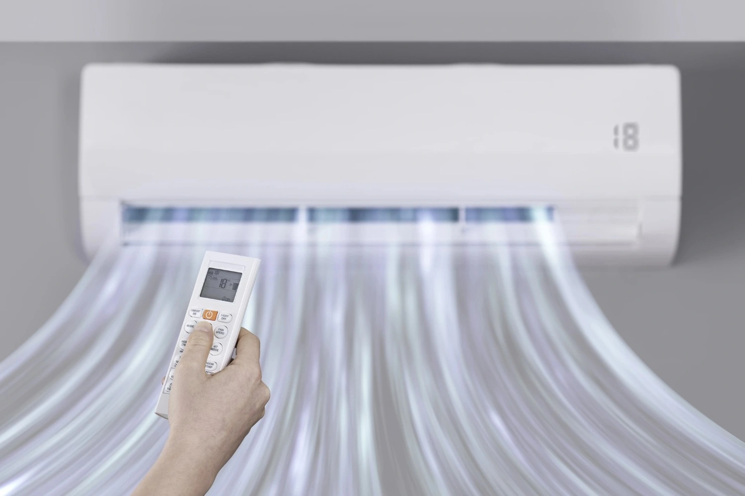 Hand holding a remote control pointing at a split air conditioner unit blowing air.