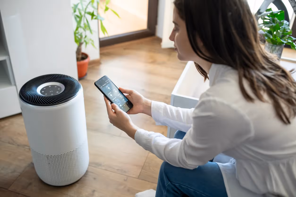 A person sits on a sofa looking at their phone next to an air purifier