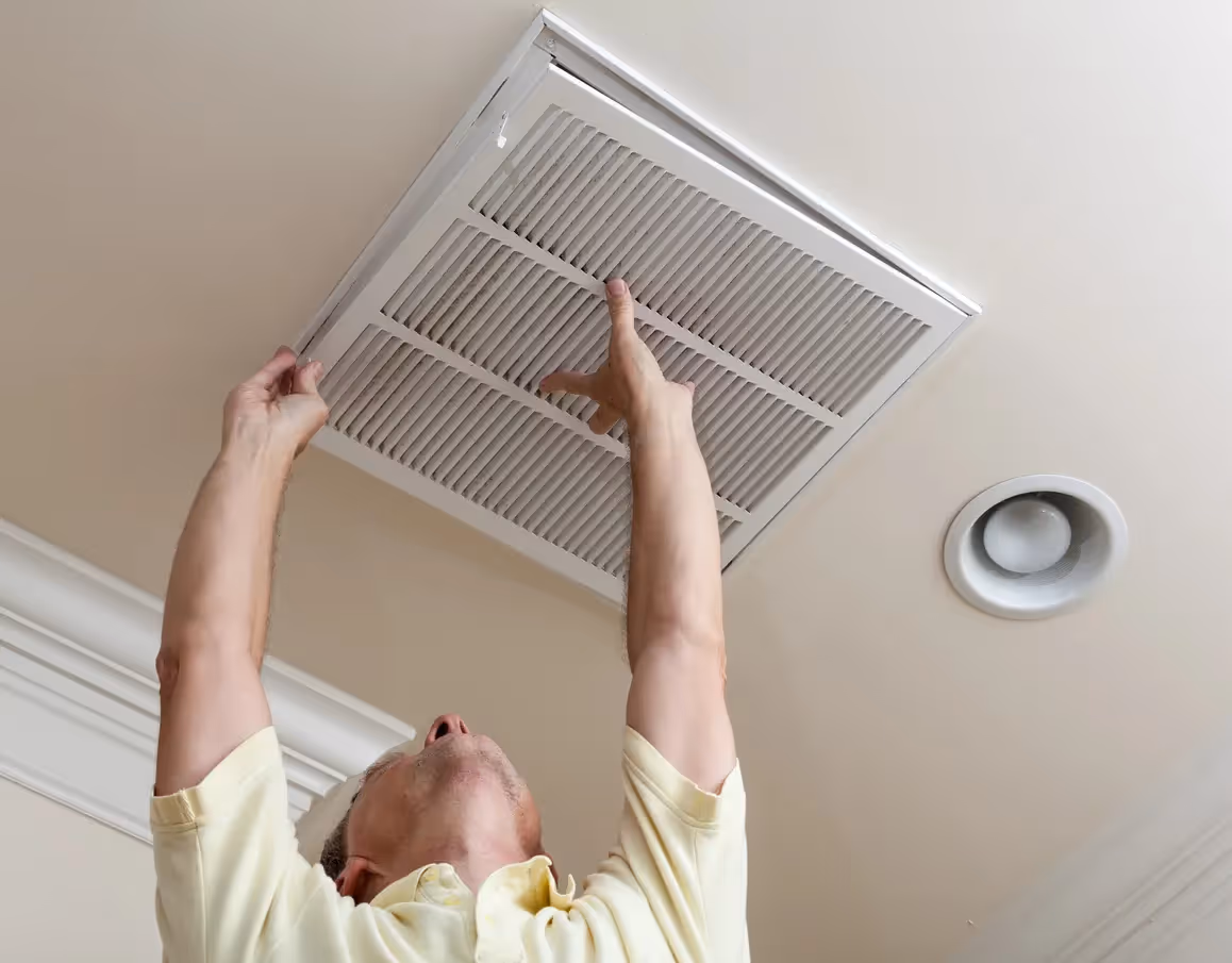 A person installs a square air filter into a ceiling ventc