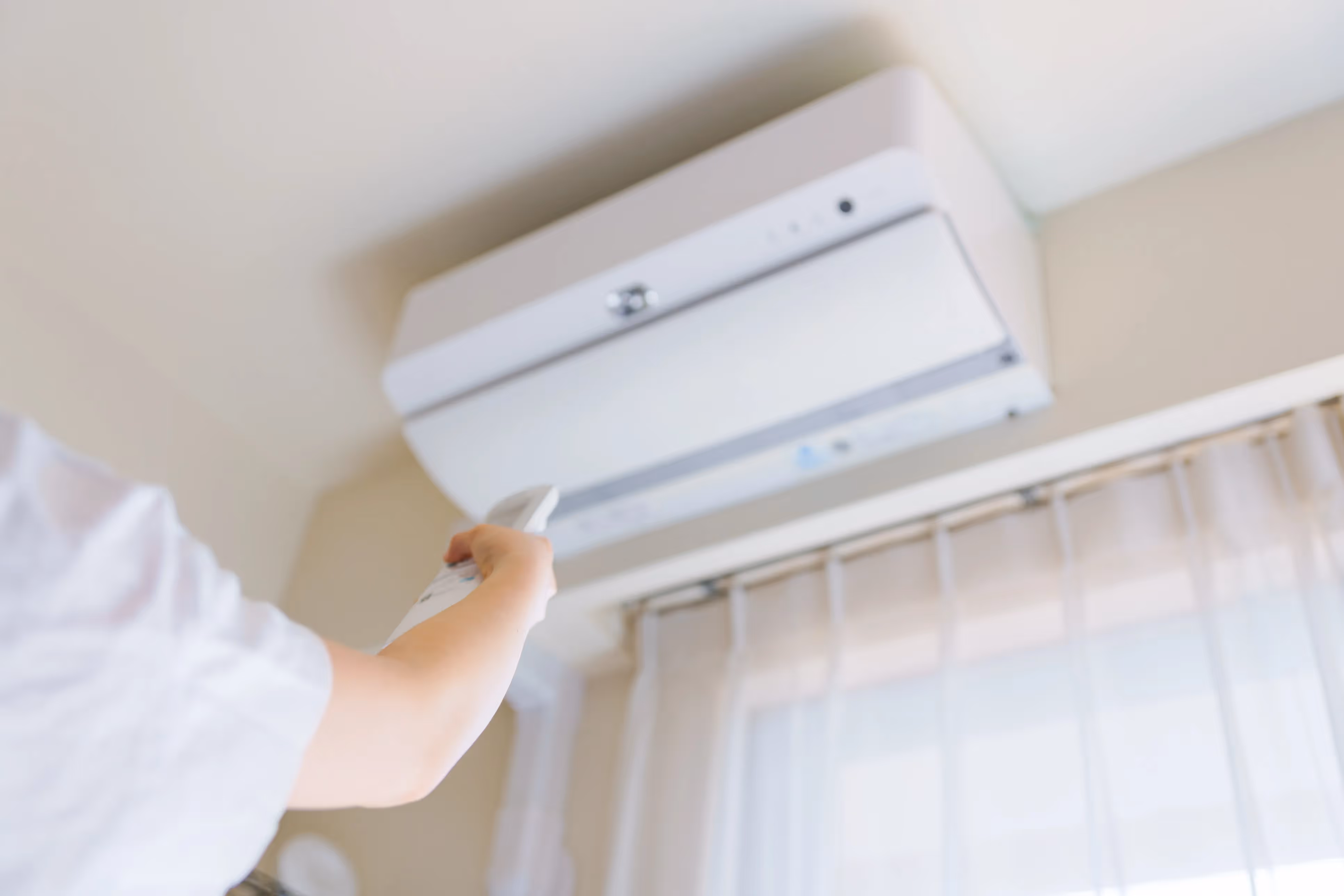A person use remote to operate a wall-mounted air conditioning unit indoors