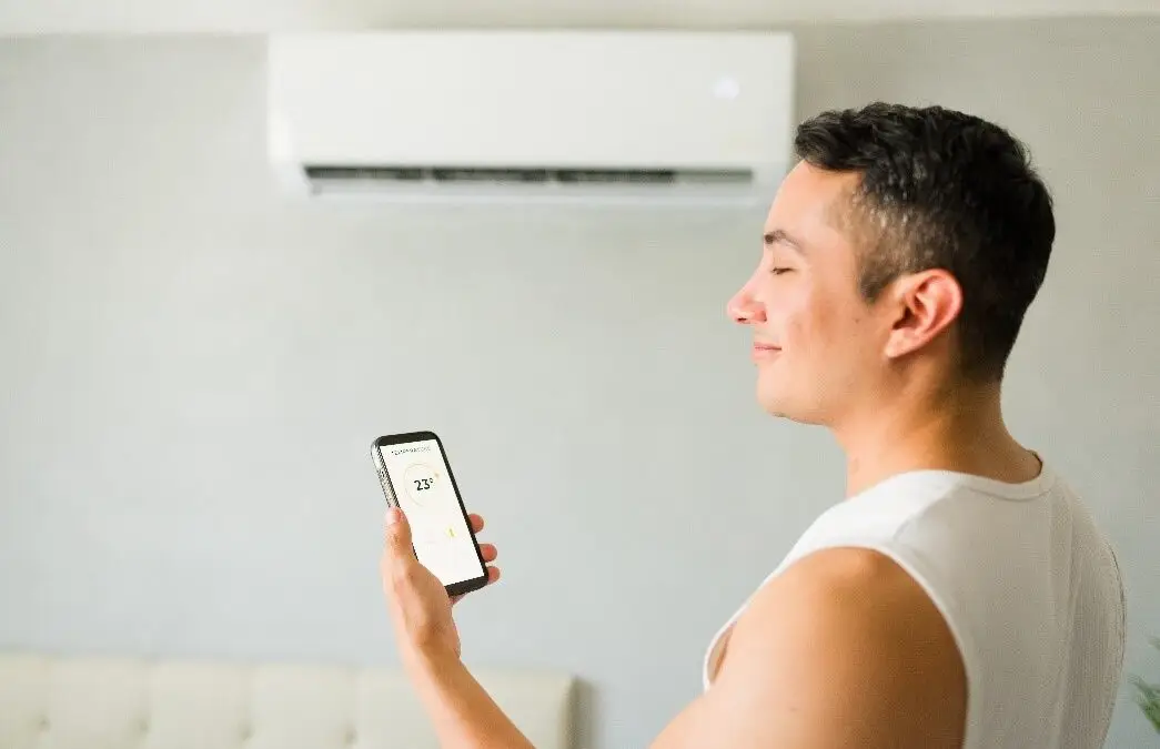 A man smiling while using a smartphone app to control a wall-mounted mini-split air conditioner.