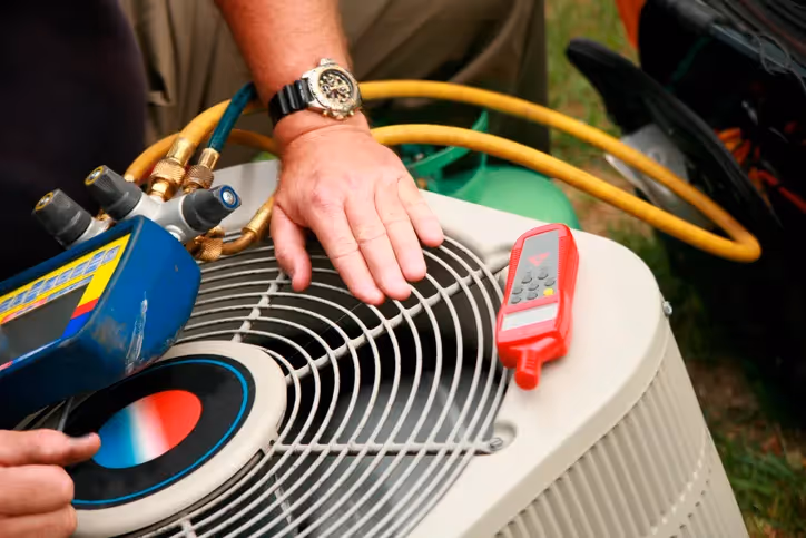 A technician checks an outdoor air conditioning unit with gauges and tools.