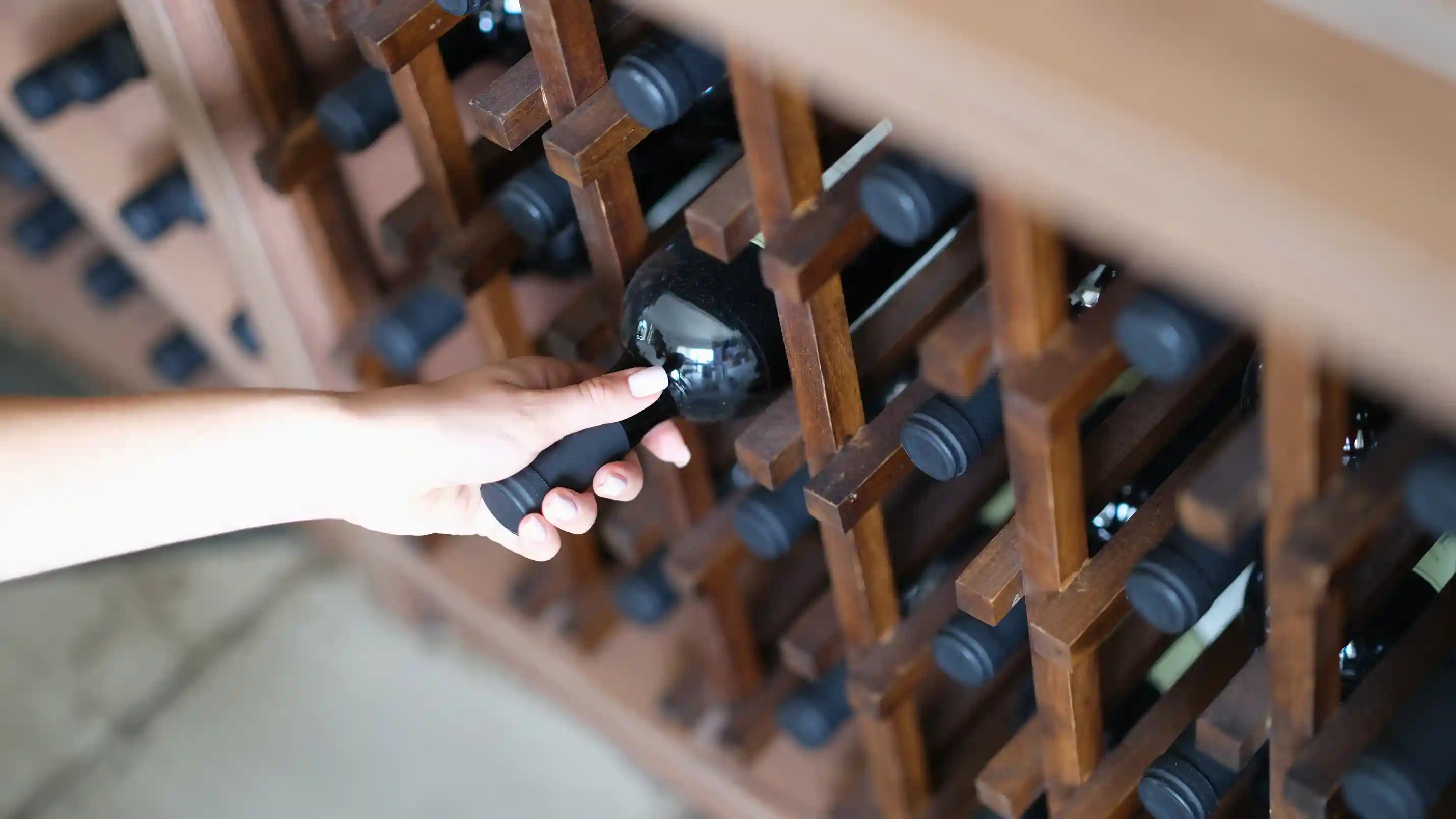 Close-up of a hand pulling a bottle of wine from a traditional wooden rack.