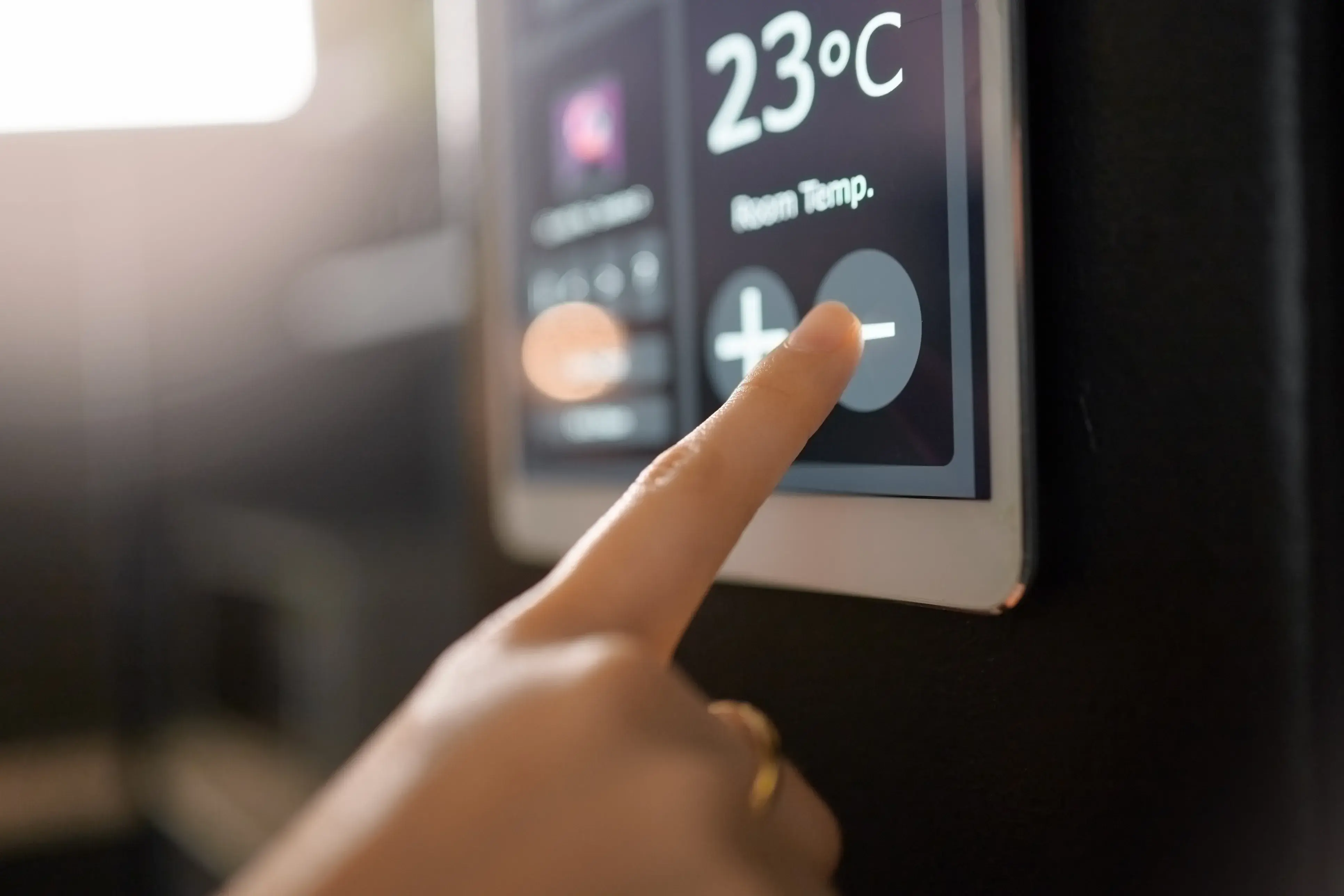 Finger pressing the temperature control on a touch-screen smart panel.