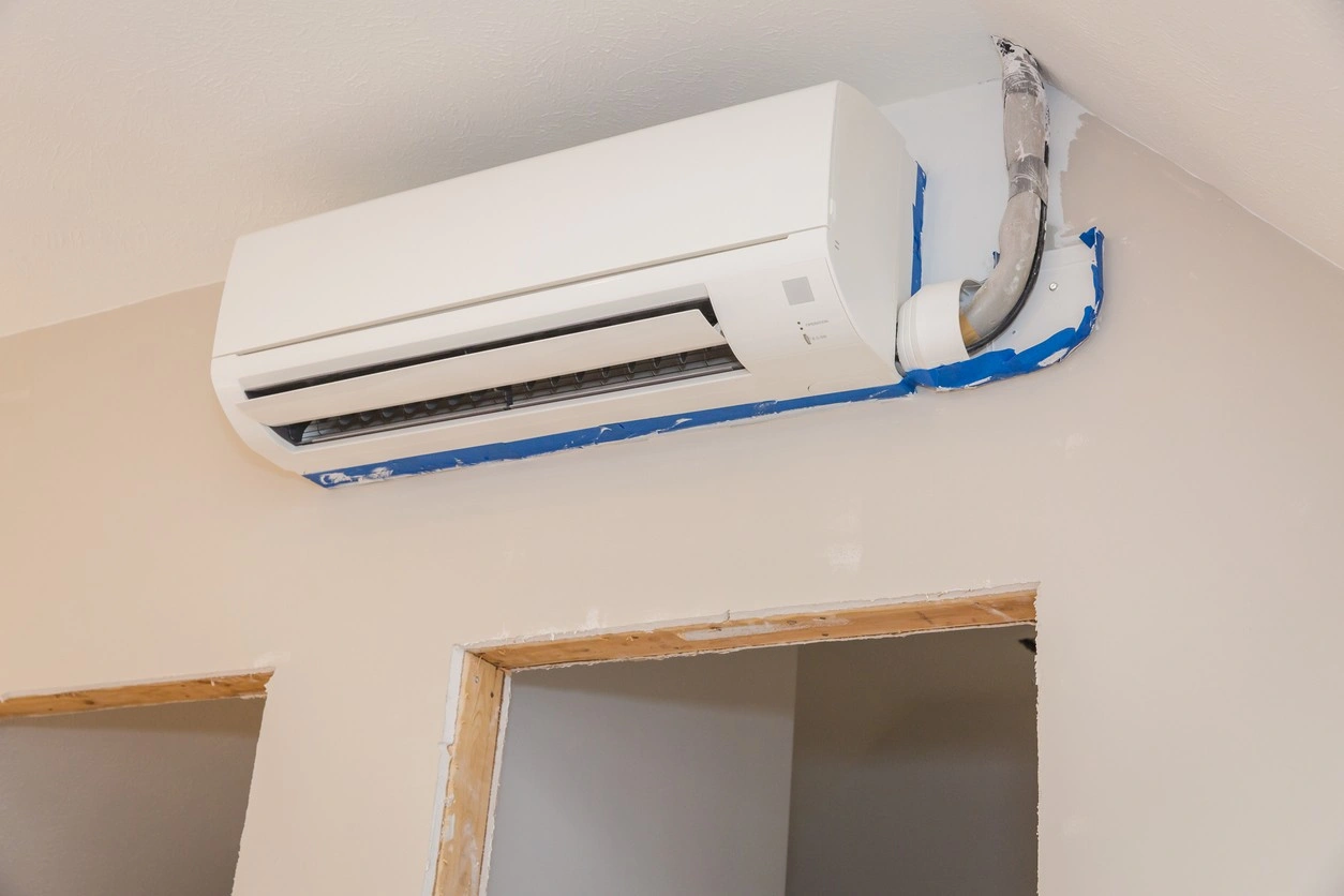 Wall-mounted mini-split AC unit installed above doorway in a room under renovation with exposed framing.